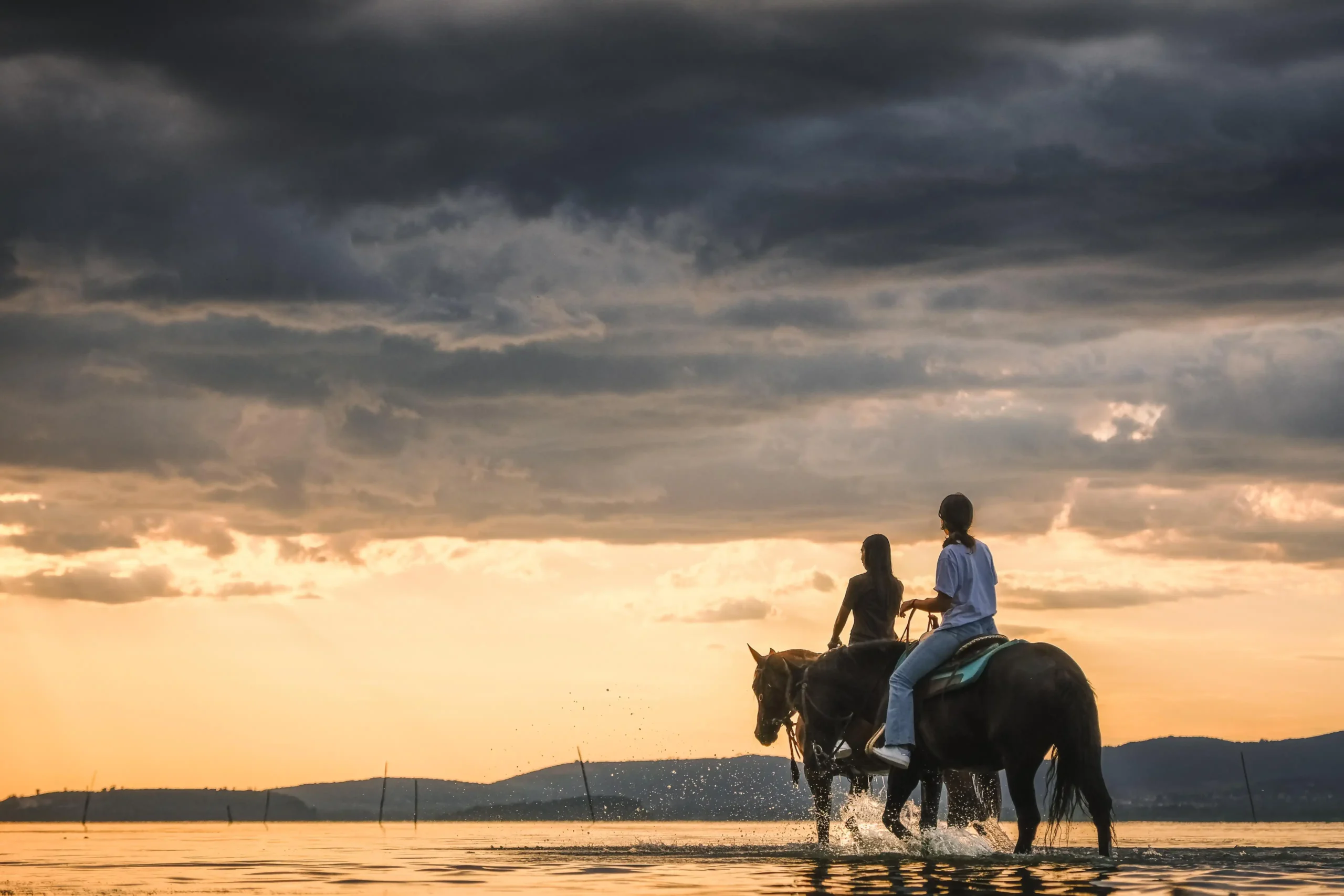 Due persone a cavallo nel lago Trasimeno durante un tramonto.