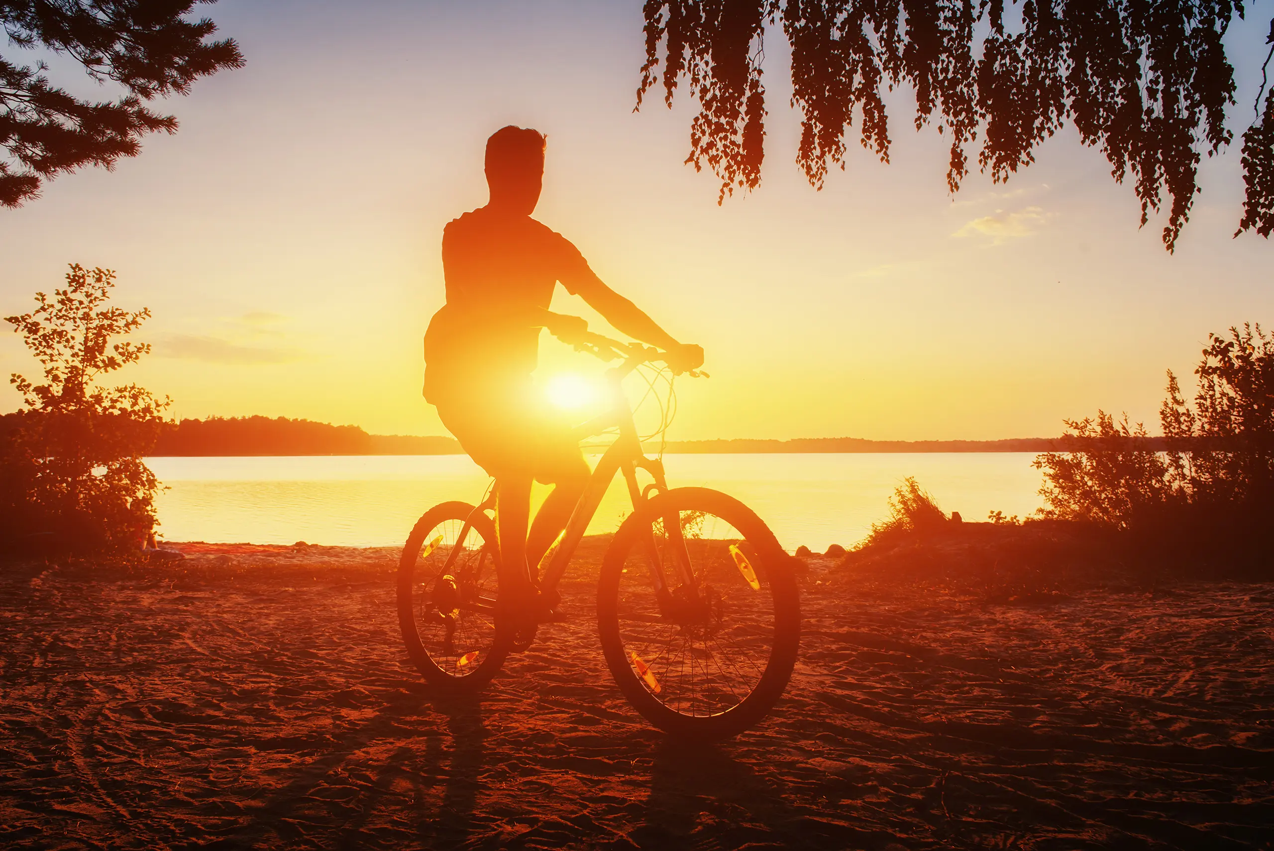 Un uomo in sella a una mountain bike sulla sponda di un lago al tramonto.
