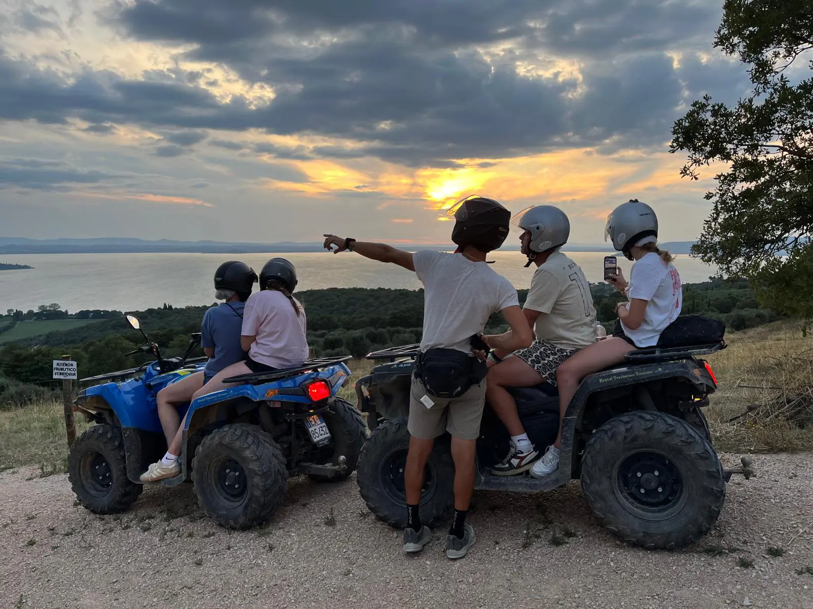 Due quad fermi in fila lungo un sentiero che percorre le colline intorno al lago Trasimeno, visibile sullo sfondo. Una persona è in piedi a fianco di uno dei due quad, mentre altre due coppie di persone sono in sella.