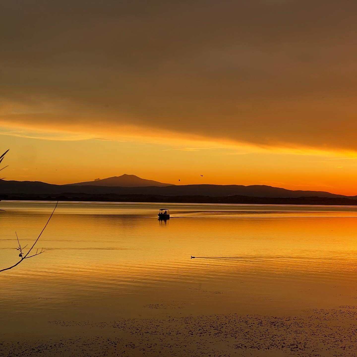 Una barca in lontananza che naviga in un lago al tramonto.