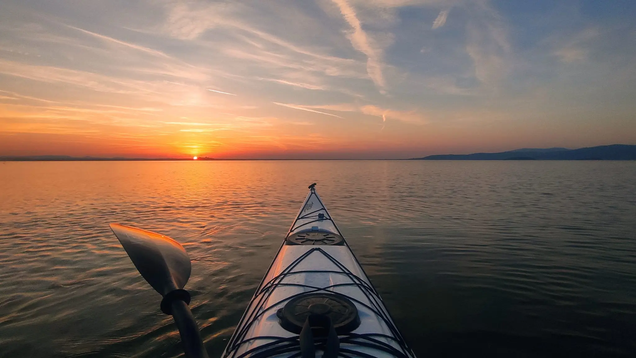 Vista in prima persona da una canoa che naviga sulle acque del lago Trasimeno al tramonto.